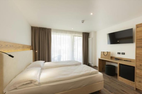 Jasny pokój hotelowy z łóżkiem małżeńskim, telewizorem i drewnianymi meblami.