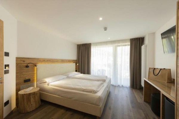 Nowoczesny pokój hotelowy z podwójnym łóżkiem, drewnianą podłogą i dużym oknem z zasłonami.