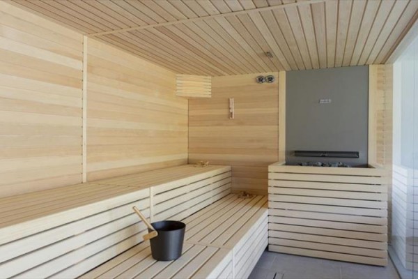 Drewniana sauna z ławkami i piecem, w rogu wiadro i chochelka na wodę.