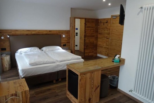 Pokój hotelowy z łóżkiem małżeńskim, drewnianymi meblami i telewizorem na ścianie.