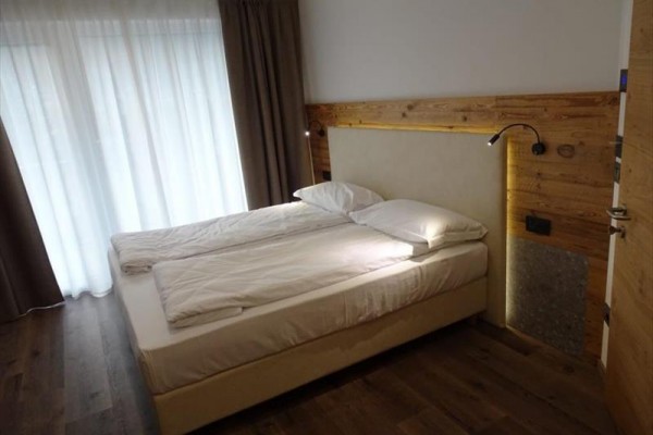 Podwójne łóżko w nowoczesnej sypialni z drewnianą podłogą i zasłonami.