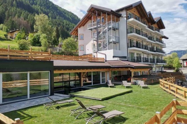Nowoczesny hotel z tarasem i leżakami na bujnym zielonym ogrodzie otoczony górami.