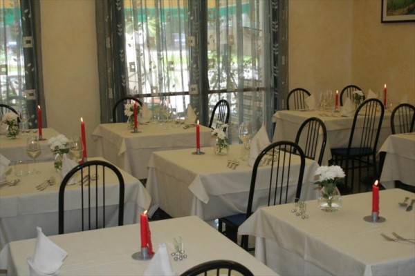 Wnętrze restauracji z nakrytymi stołami, ozdobionymi czerwonymi świecami i białymi kwiatami.