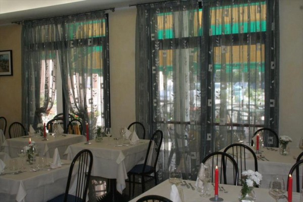 Restauracja z nakrytymi stołami, świecami i ozdobnymi zasłonami w oknach.