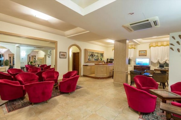 Hotelowy salon z czerwonymi fotelami, barem i telewizorem.