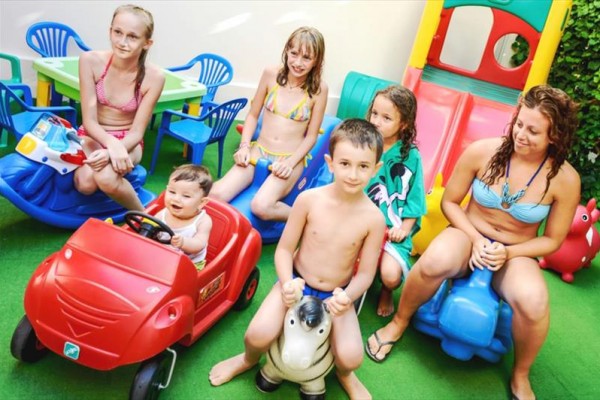 Grupa dzieci i dorosłych siedzi na zewnątrz i bawi się zabawkami.