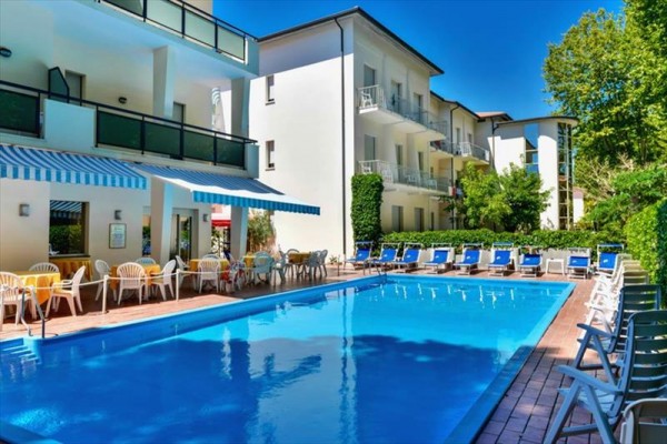 Basen przy nowoczesnym hotelu otoczony leżakami i stołami z krzesłami.