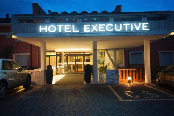 Wejście do hotelu Executive z podświetlonym napisem i zaparkowanymi samochodami.