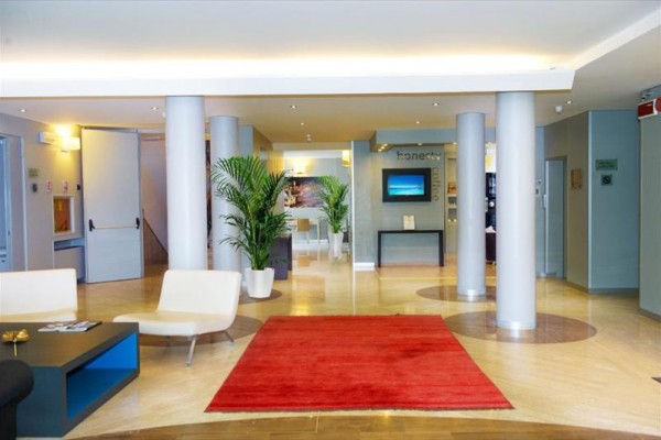 Jasna nowoczesna recepcja hotelowa z czerwonym dywanem, krzesłami i roślinami.