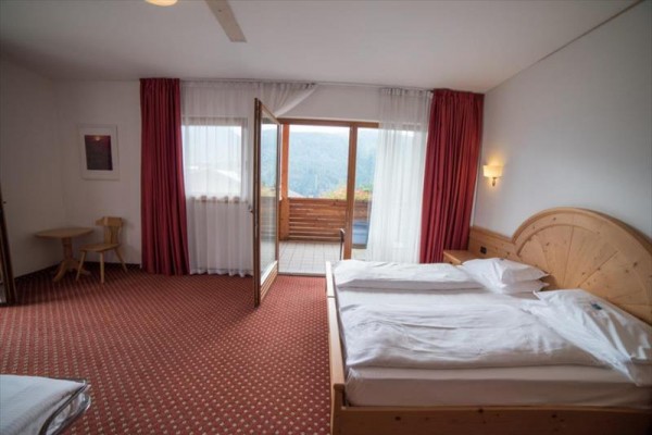 Pokój hotelowy z podwójnym łóżkiem, otwartymi drzwiami na balkon i widokiem na góry.