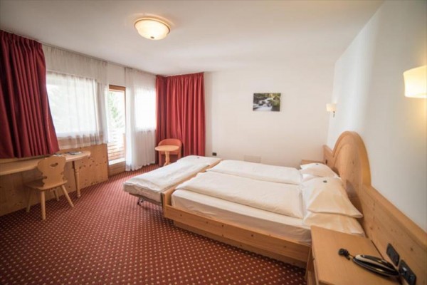 Jasny pokój hotelowy z podwójnym łóżkiem, czerwonymi zasłonami i drewnianymi meblami.
