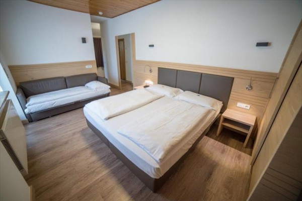 Jasny pokój hotelowy z podwójnym łóżkiem i sofą.