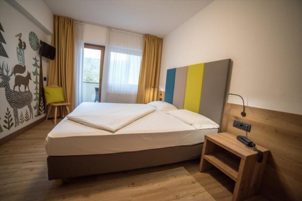 Nowoczesny pokój hotelowy z łóżkiem małżeńskim, stolikiem nocnym i malowidłem ze zwierzętami na ścianie.