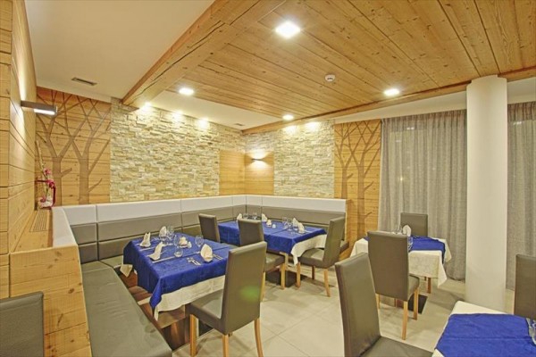 Restauracja z kamiennymi ścianami i drewnianym sufitem, z niebieskimi obrusami i szarymi krzesłami.