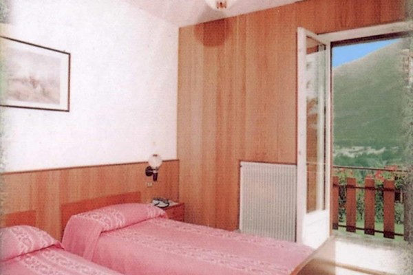 Dwa łóżka z różową pościelą w pokoju z otwartymi drzwiami na balkon z widokiem na naturę.