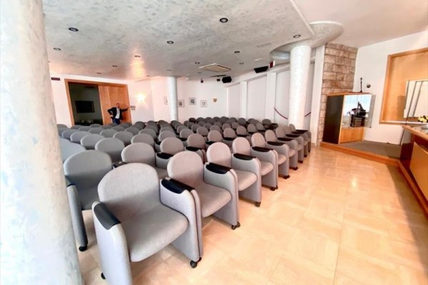 Pusta sala konferencyjna z rzędami szarych foteli.