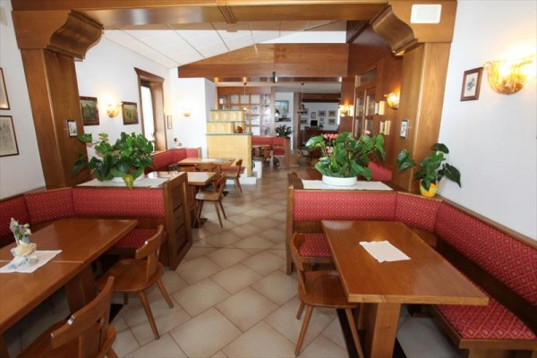 Restauracja z drewnianymi meblami i czerwonymi ławkami, ozdobiona roślinami.