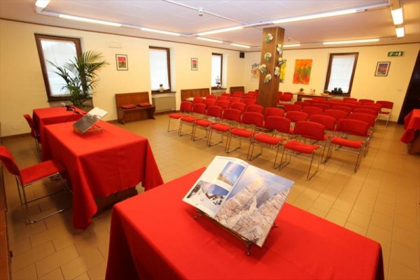 Sala konferencyjna z czerwonymi krzesłami i stołami, na których leży otwarta książka.