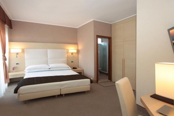 Nowoczesny pokój hotelowy z łóżkiem małżeńskim, biurkiem i telewizorem na ścianie.