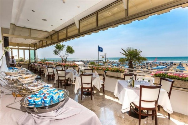 Restauracja z widokiem na plażę i morze, z nakrytymi stolikami i stołem bufetowym.