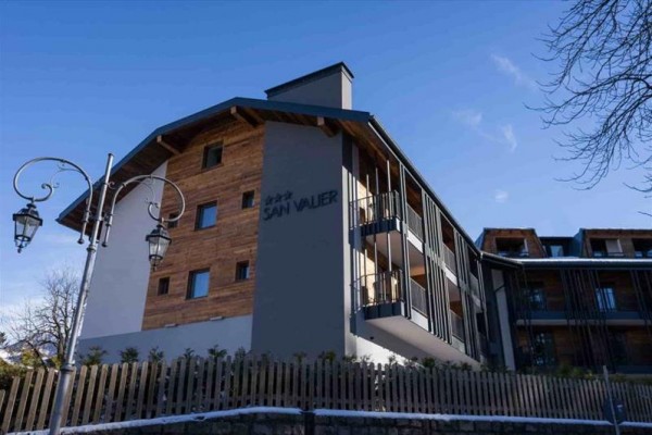 Budynek hotelowy z drewnianymi elementami i napisem San Valier, otoczony ogrodzeniem.