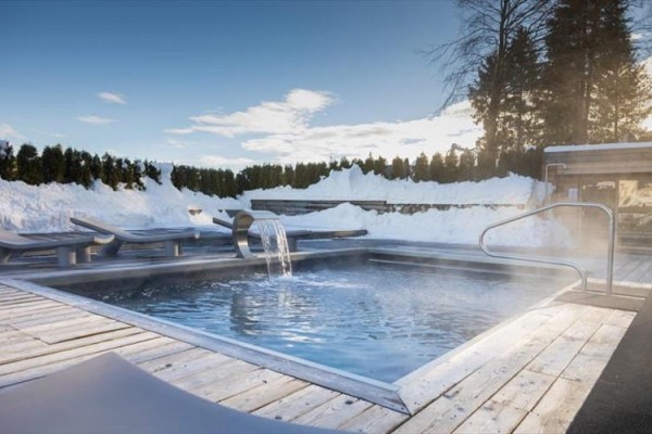 Zewnętrzny basen z jacuzzi otoczony śniegiem i leżakami.