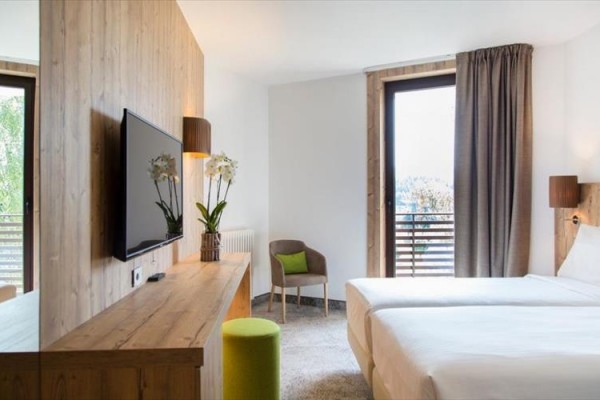 Nowoczesny pokój hotelowy z dwoma łóżkami, telewizorem i drzwiami balkonowymi.