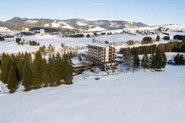Górski hotel otoczony zaśnieżonym krajobrazem i lasami.