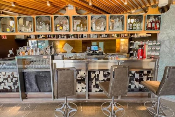 Nowoczesny bar z wysokimi krzesłami i szerokim wyborem butelek na półkach.
