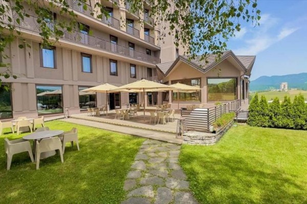 Taras hotelowy z miejscami do siedzenia i parasolami otoczony trawnikiem z widokiem na góry.