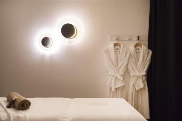 Pokój spa z stołem do masażu, dwoma szlafrokami i nowoczesnymi lampami na ścianie.