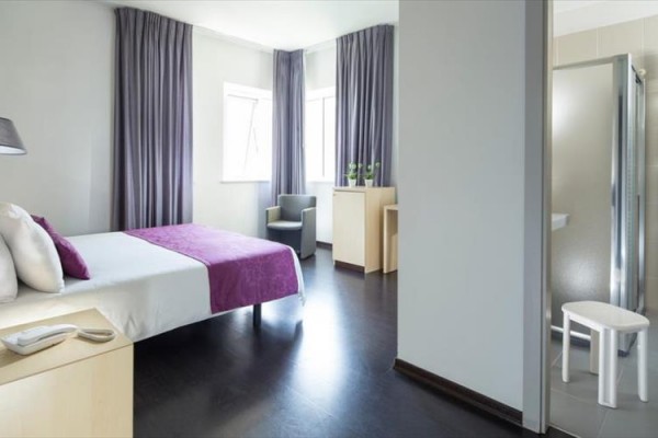 Nowoczesny pokój hotelowy z łóżkiem, fioletowymi zasłonami i kabiną prysznicową.