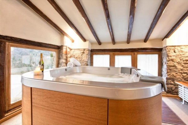 Jacuzzi w rustykalnym pomieszczeniu z drewnianymi belkami i kamiennymi ścianami.