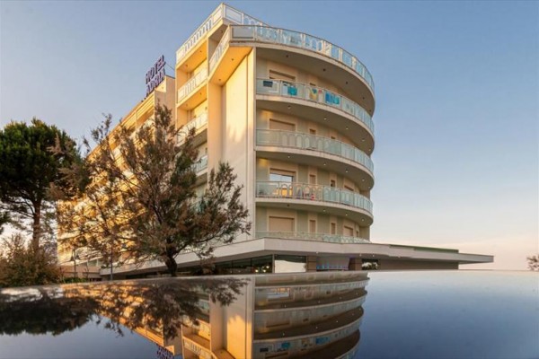 Nowoczesny wielopiętrowy budynek hotelu z balkonami otoczony drzewami o zmierzchu.