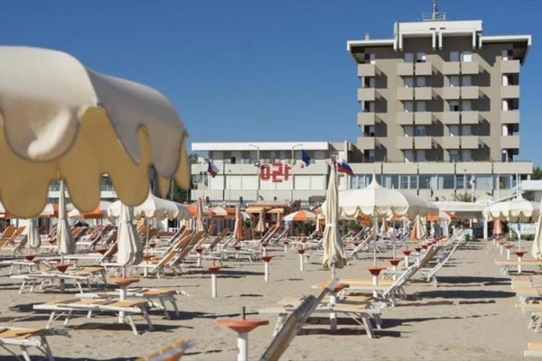 Plaża z leżakami i parasolami przed wysokim hotelem.