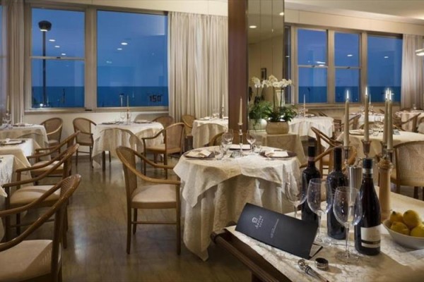 Elegancka restauracja z nakrytymi stołami, butelkami wina i widokiem na morze.