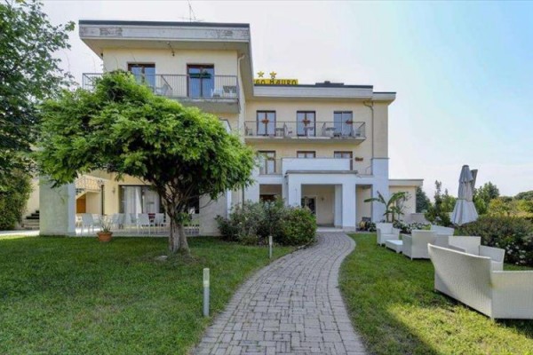 Trzypiętrowy budynek hotelu z tarasem i ogrodem z alejką i miejscem do siedzenia na zewnątrz.