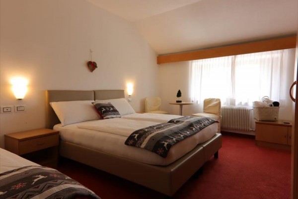 Przytulny pokój hotelowy z łóżkiem małżeńskim, stolikami nocnymi i dużym oknem.