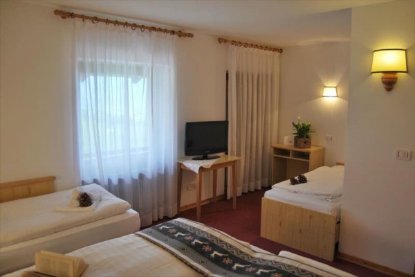 Pokój hotelowy z trzema łóżkami, telewizorem i zasłonami w oknach.