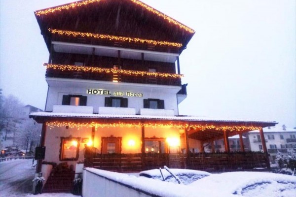 Trzypiętrowy hotel ozdobiony łańcuchami świetlnymi, zaśnieżony krajobraz.