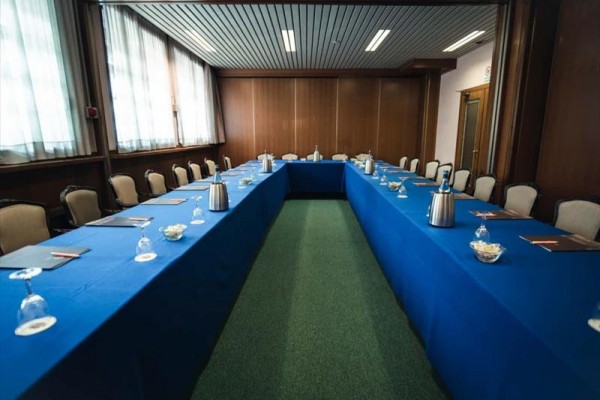 Sala konferencyjna z układem stołu w kształcie litery U z niebieskimi obrusami.