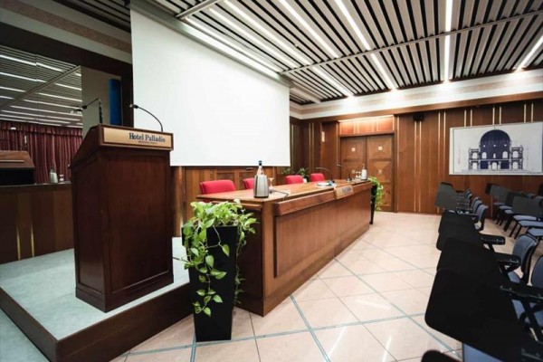 Sala konferencyjna ze stołami, krzesłami i dużym ekranem projekcyjnym.