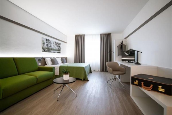 Nowoczesny pokój hotelowy z podwójnym łóżkiem, zieloną sofą i miejscem do pracy.