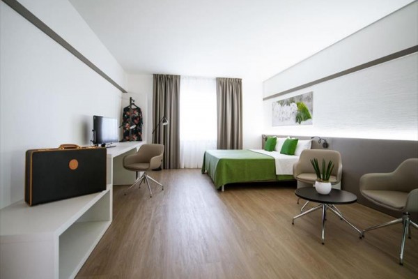 Nowoczesny pokój hotelowy z łóżkiem małżeńskim, telewizorem i fotelami.