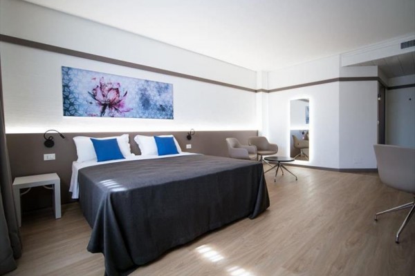 Nowoczesny pokój hotelowy z łóżkiem małżeńskim, dwoma fotelami i obrazem nad łóżkiem.