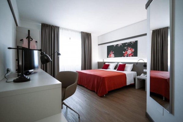 Nowoczesny pokój hotelowy z podwójnym łóżkiem, biurkiem i dużym lustrem.