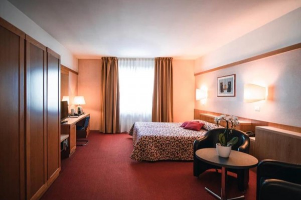 Pokój hotelowy z podwójnym łóżkiem, biurkiem i fotelami ze stolikiem.