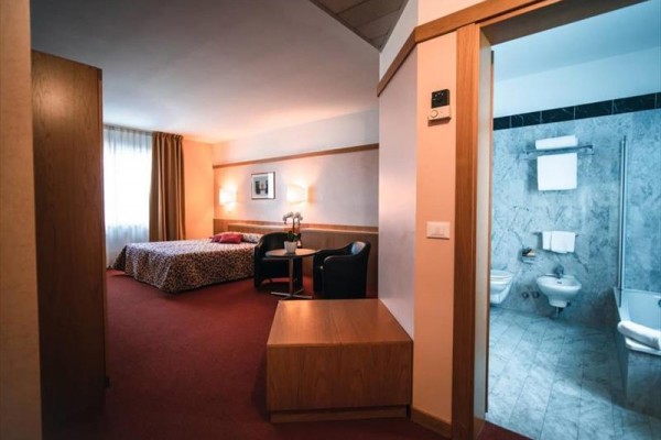 Pokój hotelowy z łóżkiem małżeńskim i przyległą łazienką z marmurowymi płytkami.