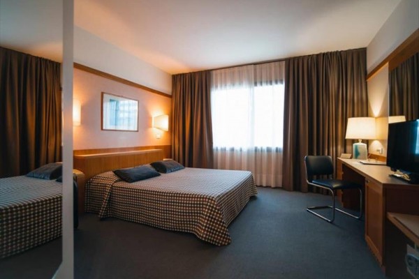 Pokój hotelowy z łóżkiem dwuosobowym, biurkiem i zasłonami na oknach.