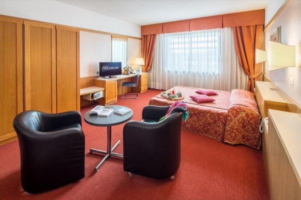 Pokój hotelowy z łóżkiem małżeńskim, dwoma fotelami, stolikiem i stanowiskiem pracy z komputerem.